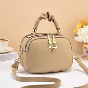 Chic beige crossbody bag with gold bow charm and ruched handle on a minimalist background