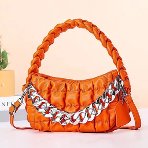 Detail of bright orange quilted bag with chunky silver chain and woven handle