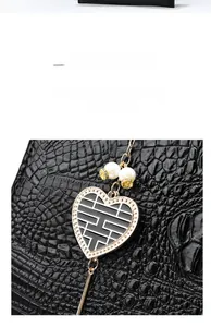 Detail of black crocodile texture tote bag with heart charm and pearl accents