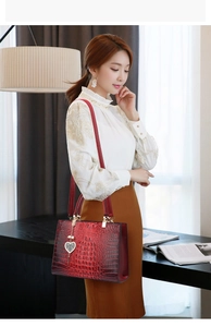 Close-up of deep red crocodile embossed leather tote with heart pearl charm detail