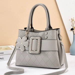 Detail of grey quilted leather tote bag featuring rhinestone buckle and floral charm