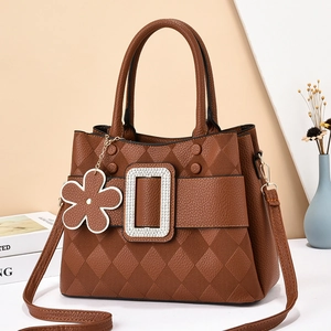 Brown leather tote bag with rhinestone buckle and floral pendant in a stylish setting