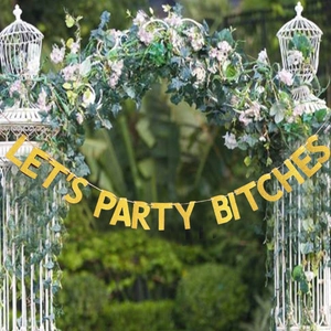 Gold glitter Let's Party Bitches banner hanging on an outdoor garden flower arch