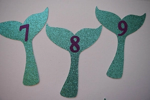 Detail of glitter mermaid tail photo banners with purple numbers for baby birthday party