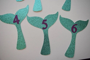 Detail of glitter mermaid tail photo clips with purple numbers for birthday decor