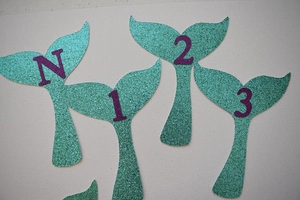 Detail showing glitter mermaid tail photo clips with purple numbers for party banners