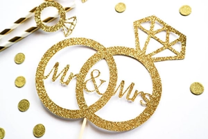 Close-up of glittery gold Mr & Mrs cake topper with interlocked rings and diamond design