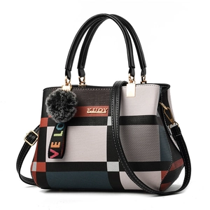 Detail view of plaid patterned handbag with plush ball pendant and gold logo