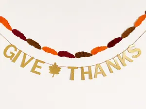 Close-up of Give Thanks gold glitter banner with autumn maple leaves and colorful feathers
