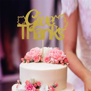 Close-up of gold glitter Give Thanks cake topper with maple leaves on a white cake