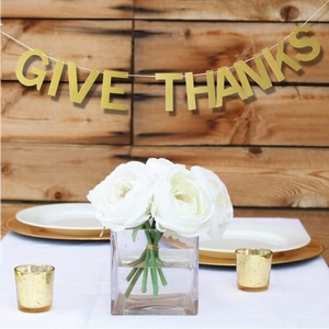 Close-up of glittery golden Give Thanks banner hanging over a Thanksgiving table setup