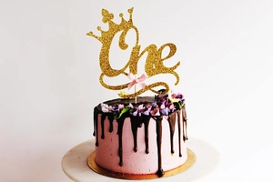 Macro detail of golden glitter One cake topper with crown and pink silk bow decoration