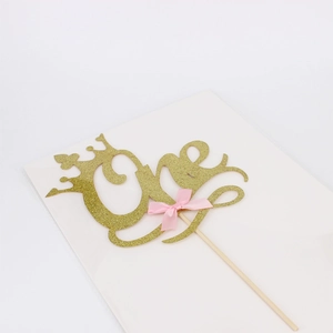 Golden glitter 'One' cake topper with crown and pink bow for first birthday party decor
