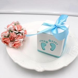 Detail of baby shower favor box with hollow footprint design and blue silk bow on white plate