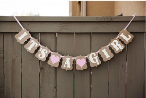 Macro shot of IT'S A GIRL kraft paper banner with pink heart and ribbon on wooden fence
