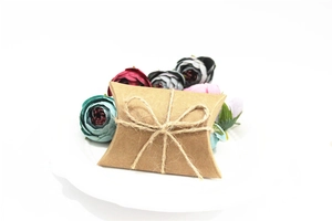 Detail of kraft paper pillow gift box with hemp rope bow on white ceramic plate