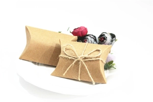 Macro view of kraft paper pillow boxes with twine bows on a white ceramic plate