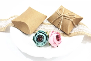 Detail of vintage kraft paper pillow boxes with twine bow on white ceramic plate