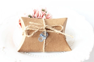 Detail of kraft paper pillow gift box with jute twine and a blue mini pacifier charm