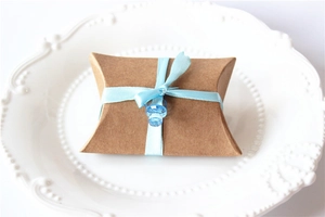 Kraft paper pillow gift box with light blue ribbon and a small pacifier charm detail