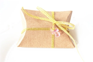 Detail of kraft pillow candy box with gold ribbon and pink pacifier charm for baby gifts