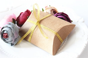 Close-up of kraft paper pillow gift box with golden ribbon bow and floral background