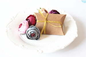Brown kraft paper pillow gift box on white plate with gold ribbon and floral decor