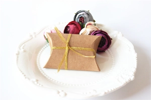 Macro shot of pillow-shaped kraft paper gift box with gold ribbon on white plate