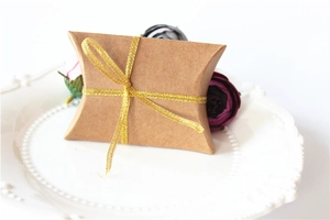 Macro shot of kraft paper pillow gift box with gold ribbon on white floral plate