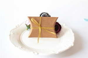 Detail of kraft paper pillow candy box with gold ribbon on a white ceramic plate