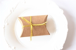 Detail view of a kraft paper pillow gift box with a golden glitter ribbon bow on a white plate