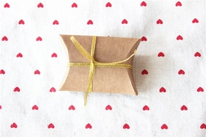 Close-up of pillow-shaped kraft paper wedding gift box with gold ribbon on heart fabric