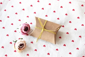 Kraft paper pillow gift box with golden ribbon on heart pattern linen background
