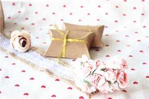 Detail of kraft paper pillow boxes with gold ribbon on floral background for wedding favors