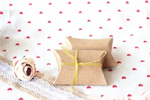 Close-up of kraft paper pillow gift boxes with gold ribbon on romantic lace background