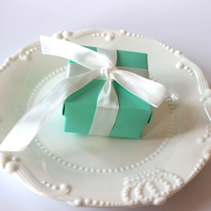 Close-up of a Tiffany blue square gift box with a white satin ribbon on a ceramic plate
