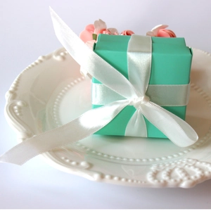 Elegant Tiffany blue square candy gift box with white satin ribbon on a vintage ceramic plate