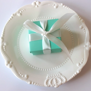 Top view of a square Tiffany blue gift box with a white satin ribbon and bow on a plate