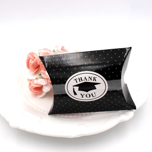 Close-up of black polka dot pillow candy box with graduation thank you label on a white plate