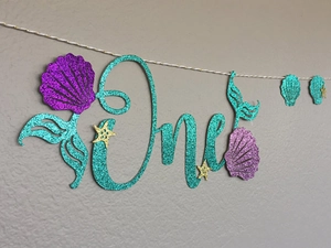 Close-up of glitter mermaid-themed 'One' banner with starfish and shell details