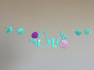 Detail of glitter Mermaid 1st birthday banner with One typography and seashell accents