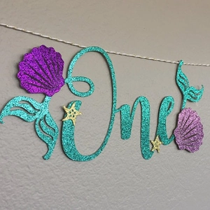 Glittery mermaid-themed 'One' banner with teal seashell and golden starfish decor