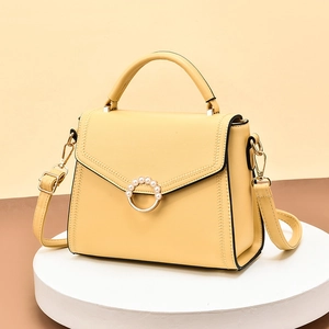 Pale yellow leather tote bag with pearl buckle on white pedestal against dual-tone background