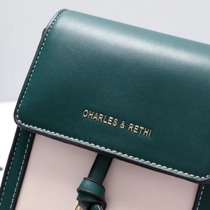 Close-up of litchi texture faux leather and gold logo on the green bicolor crossbody bag