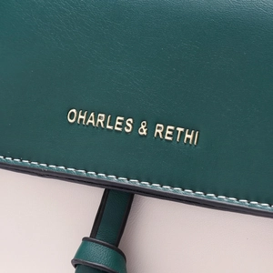 Close-up of contrast stitching and gold logo on green and beige faux leather bag