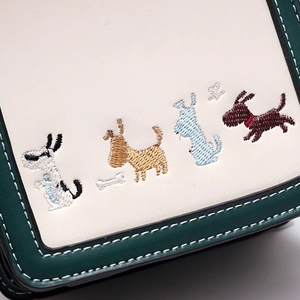 Detail of embroidered cartoon puppy patterns and contrast stitching on crossbody bag