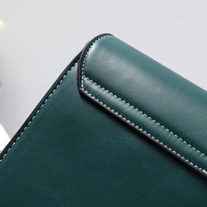 Detail of dark green leather shoulder bag with lychee texture and white stitching