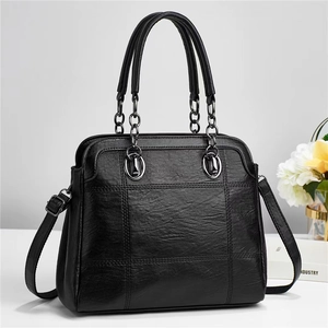 Close-up of black quilted tote bag with metallic chain handles and adjustable strap