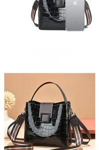 Size comparison of a black faux crocodile bucket bag with striped strap and top handle