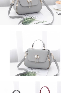 Detail of light gray crossbody bag featuring a pearl kitten charm and lychee texture